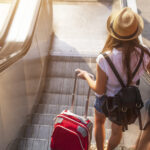 Young,Girl,With,Suitcase,Down,The,Escalator.